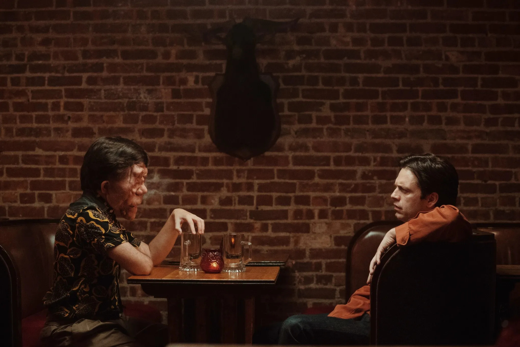 Adam Pearson and Sebastian Stan sit across from each other in a stall in a restaurant in A Different Man.