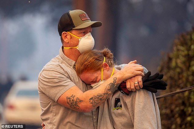 People hug each other as they return to the house after it was burned down by wildfires in the Los Angeles area