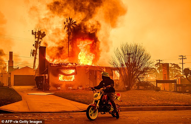 A motorcyclist stops to look at a burning house during the Eaton fire