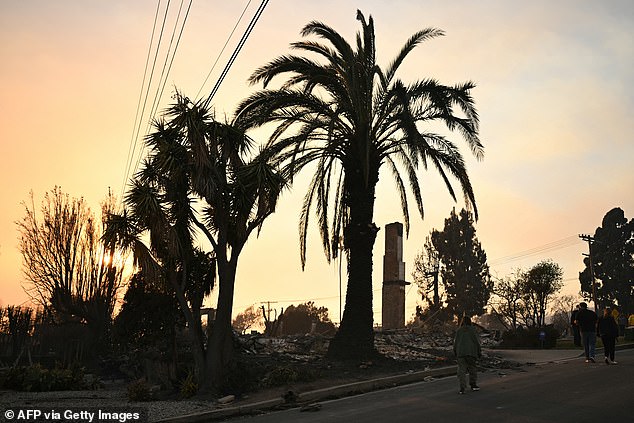 Residents walk past a burned home after searching for belongings in their home during the Palisades Fire in Pacific Palisades on Thursday