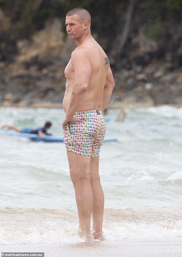 Former Myer model Kris, 46, showed off his beach body, revealing his black panther tattoo on the back and writing ink on his chest in a pair of colorful board shorts