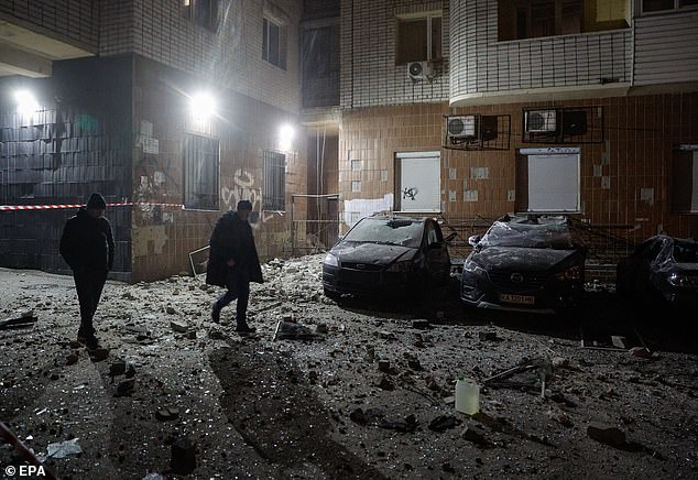 Local people walk near damaged cars at the site where drone debris falls on a residential building, in Kiev, Ukraine, January 10, 2025