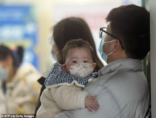 Scenes of hospitals flooded with people in face masks are making the rounds on social media. Pictured, a baby wearing a face mask waits with relatives at the pediatric ward of a hospital in Hangzhou, eastern China, on January 6