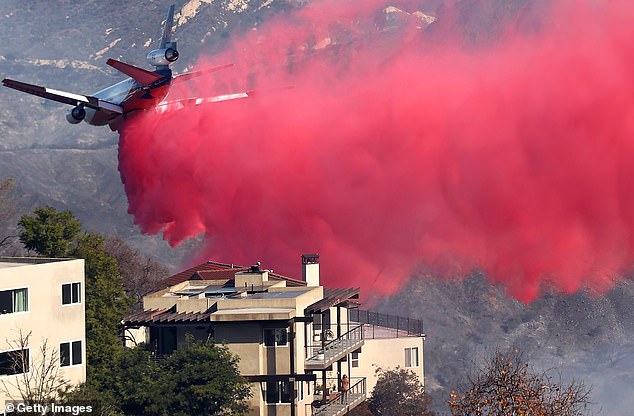 A person watches from a balcony as a firefighting plane drops fire retardant Phos-Chek near homes during the Palisades Fire