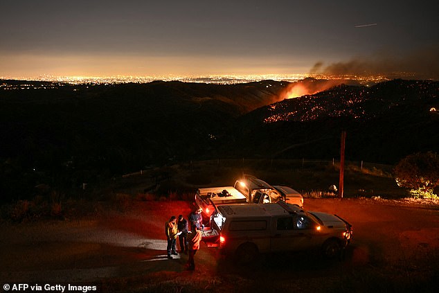 The downtown Los Angeles skyline is seen in the far left distance as firefighters monitor the Palisades fire near the Mandeville Canyon neighborhood and Encino, California on January 11