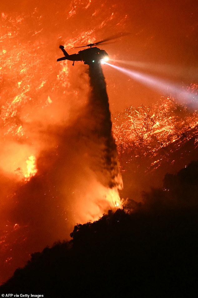 A firefighting helicopter drops water as the Palisades fire grows near the Mandeville Canyon neighborhood and Encino, California, on January 11, 2025