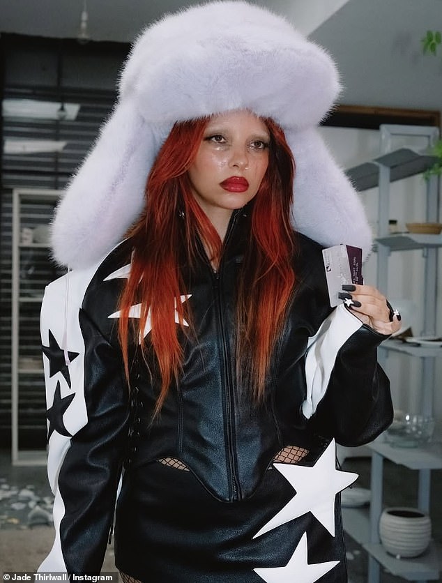 Jade wore a bold red wig and a striking large white fur hat during some scenes as she danced in a room with broken dishes on the floor