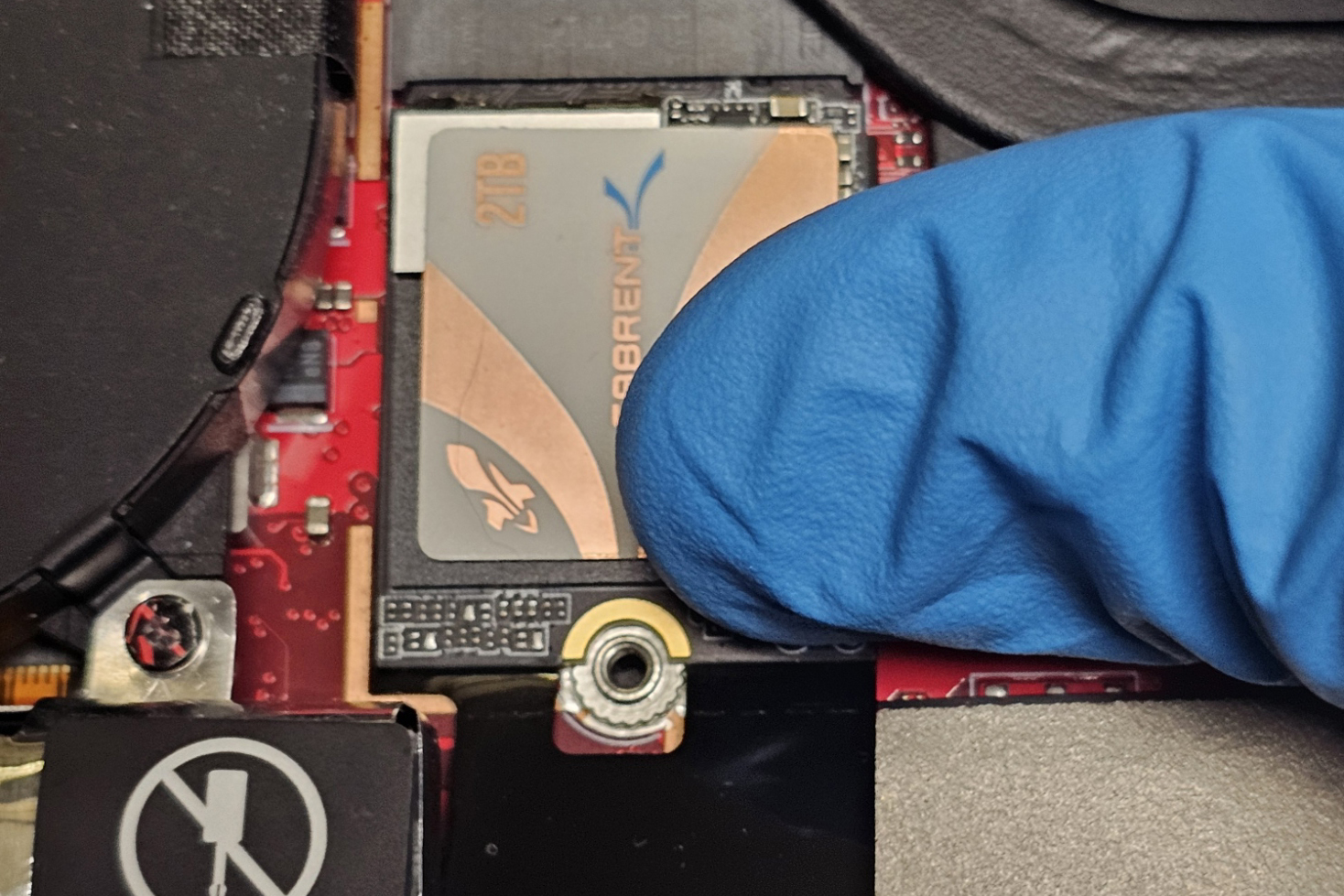 A photo of a thumb securing an M.2 SSD into the ROG Ally's M.2 socket