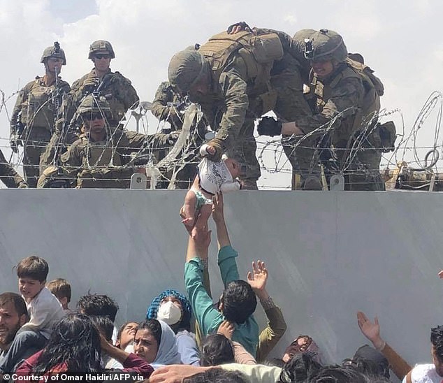 A U.S. Marine grabs a child from the crowd below during the frantic U.S. withdrawal from Afghanistan in August 2011. The withdrawal dented President Joe Biden's approval ratings for the remainder of his term.