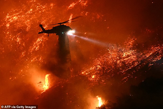 A firefighting helicopter drops water as the Palisades fire grows near the Mandeville Canyon neighborhood and Encino, California, on January 11