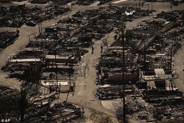 Two people walk along a road in a fire-ravaged community in the aftermath of the Palisades Fire in the Pacific Palisades neighborhood of Los Angeles, Monday, January 13, 2025