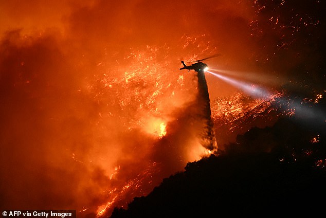 A firefighting helicopter drops water as the fire grows in the Palisades