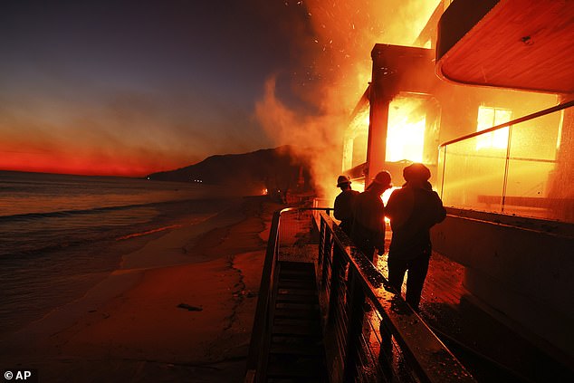 Firefighters work from a deck as the Palisades Fire burns a beachfront property in Malibu