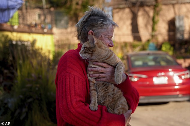 Pictured: An Altadena homeowner clutches her cat after the fire ripped through her neighborhood