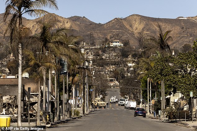 A house, seemingly unaffected by the Palisades Fire, stands on a hill amid the charred remains of other homes destroyed by the blaze as National Guard soldiers guard a checkpoint below in the Pacific Palisades neighborhood of Los Angeles, California