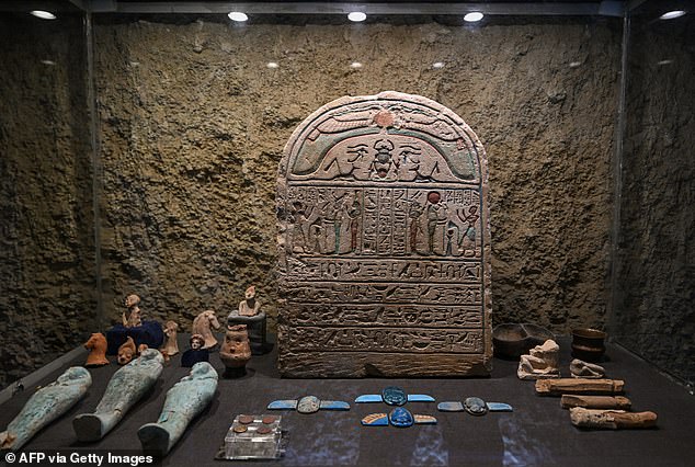 Exhibition of children's dolls and toys made of clay (back left corner), bronze coins engraved with images of Alexander the Great (center front) and winged scarabs (center front) found in the rock-cut tombs.