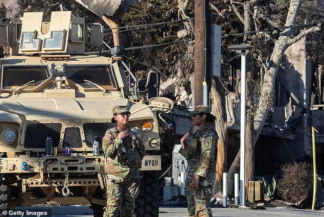 National Guard soldiers stand at a checkpoint on Sunset Boulevard, with burned homes in the background due to the Palisades Fire