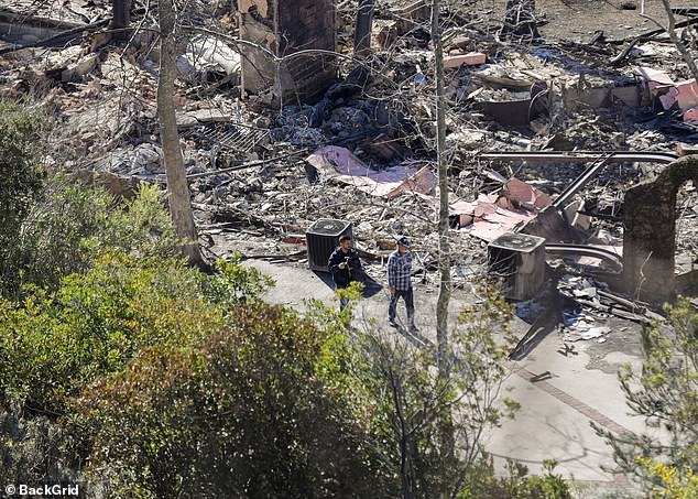 Mel Gibson walks with the remains of his destroyed Malibu home on Wednesday