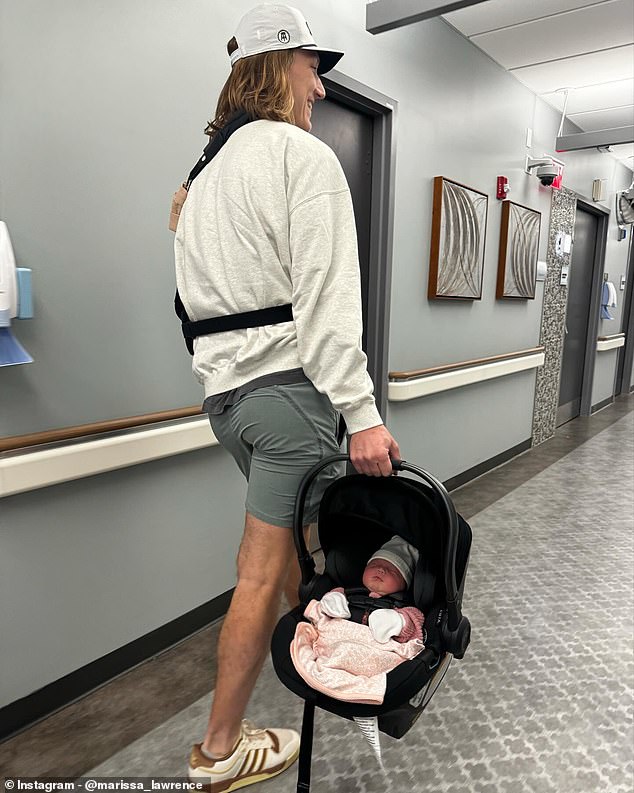 Lawrence, shown wearing a sling around his left arm, carries the baby out of the hospital with his right hand