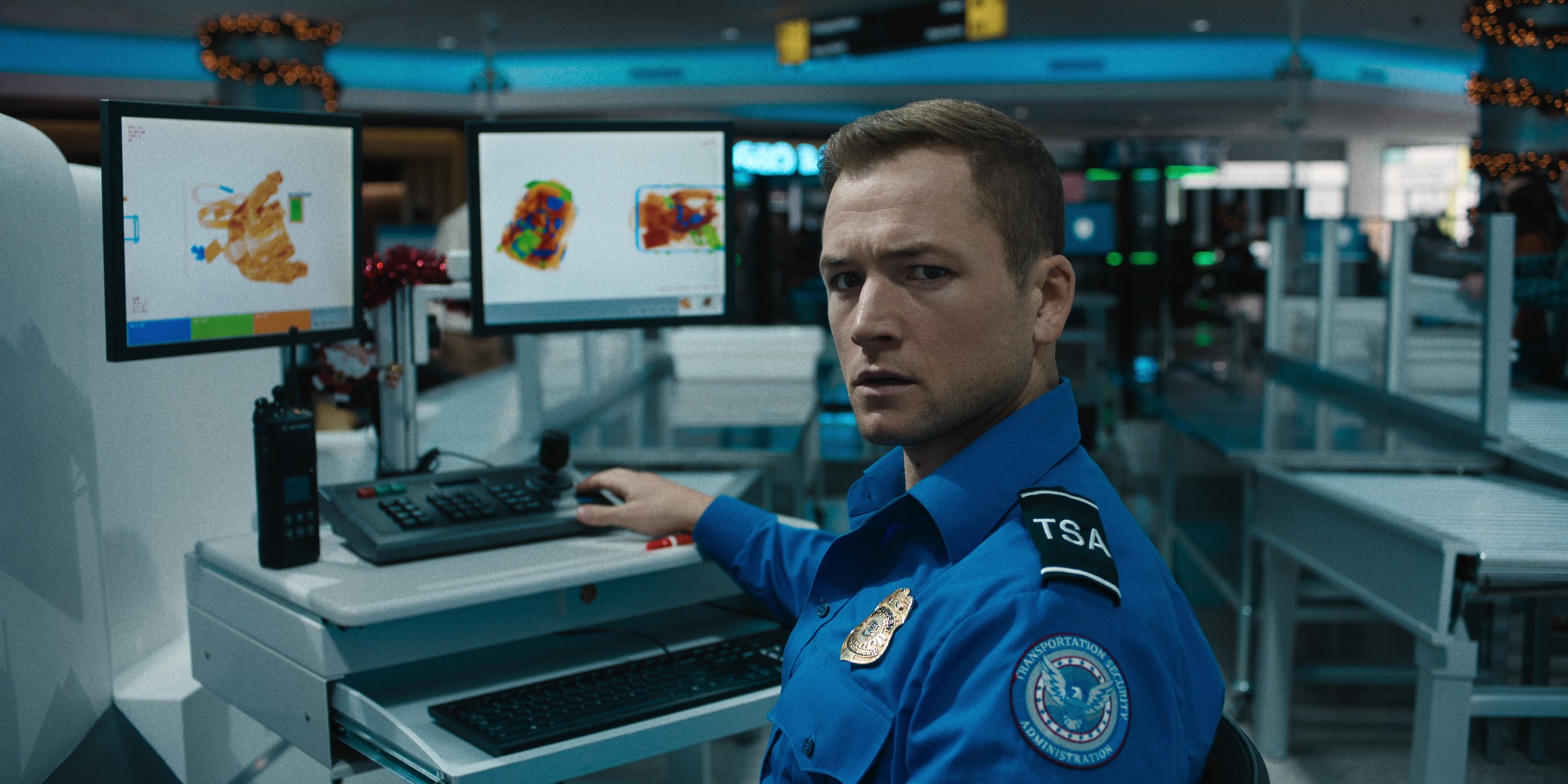 Taron Egerton as a TSA agent in Carry-On, sitting at an X-ray machine