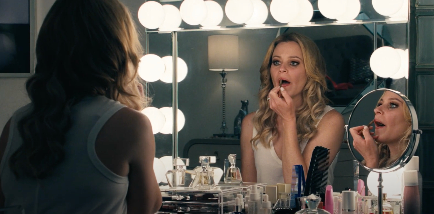 Elizabeth Banks applies makeup in a mirror in Skincare